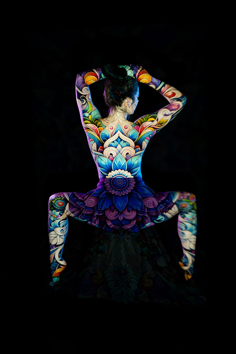 Woman sitting with her back and arms covered in colorful floral body art, set against a black background