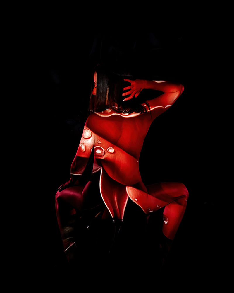 Nude person crouching with back turned, covered with red and white light projections resembling abstract patterns and droplets, set against a black background