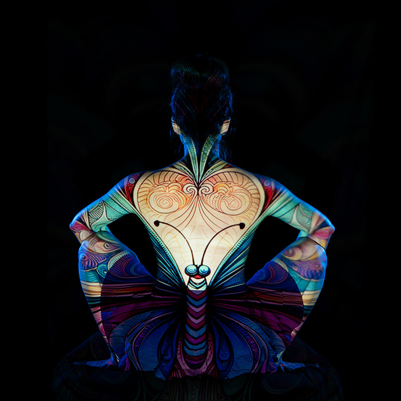 Back view of a seated person with colorful butterfly and abstract patterns projected on their body against a black background