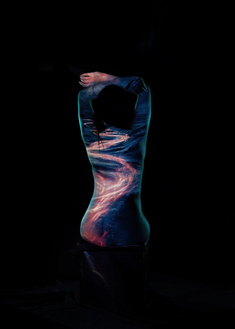 Silhouette of a person sitting with arms raised behind their head, illuminated with projected swirling light patterns in blue and pink hues against a black background