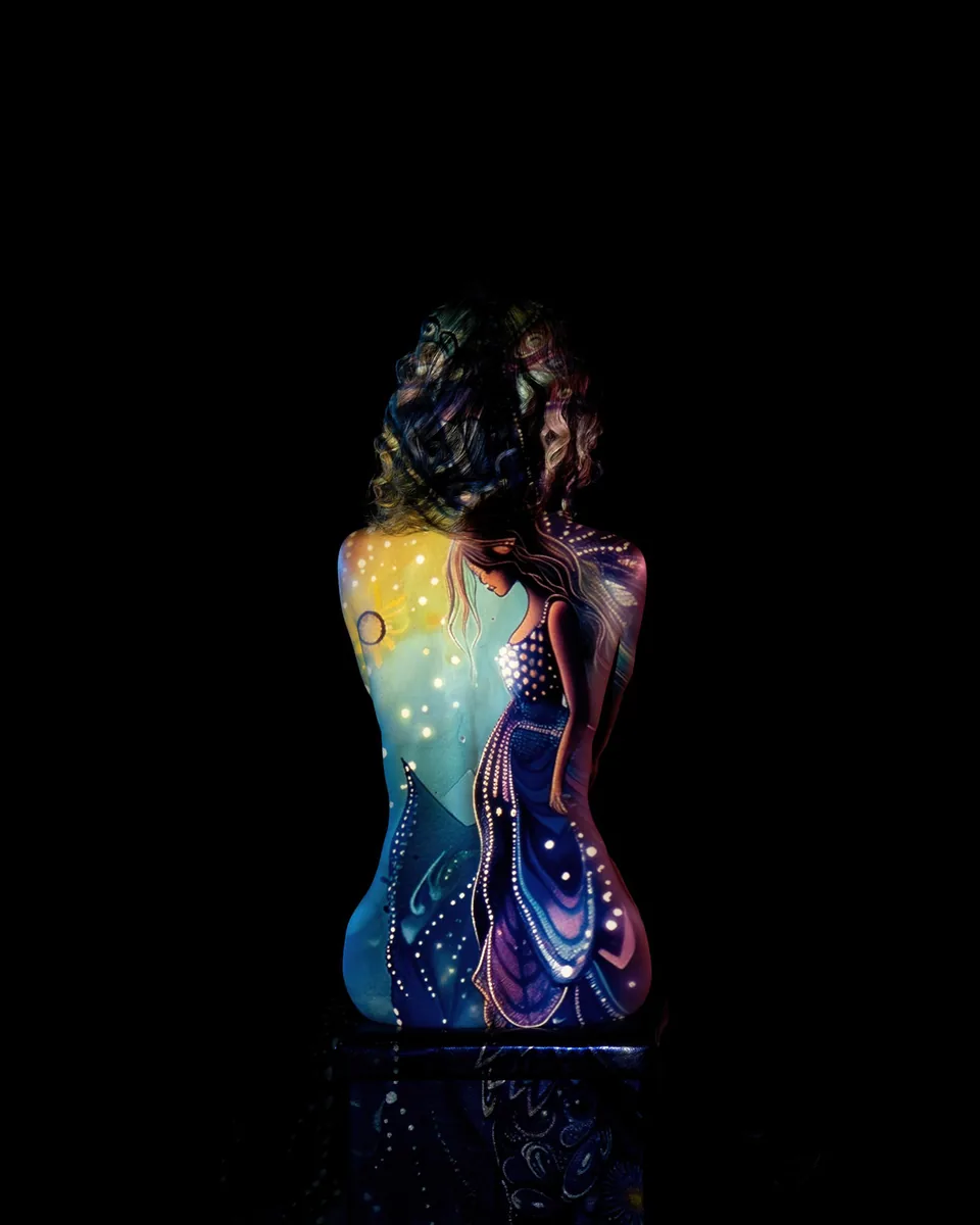 A figure sits with their back to the camera, illuminated by soft, colorful projected artwork depicting a woman in a flowing dress against a dark background.