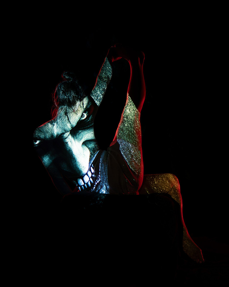 Person in a backbend pose with a large menacing face projected onto their body, set against a dark background