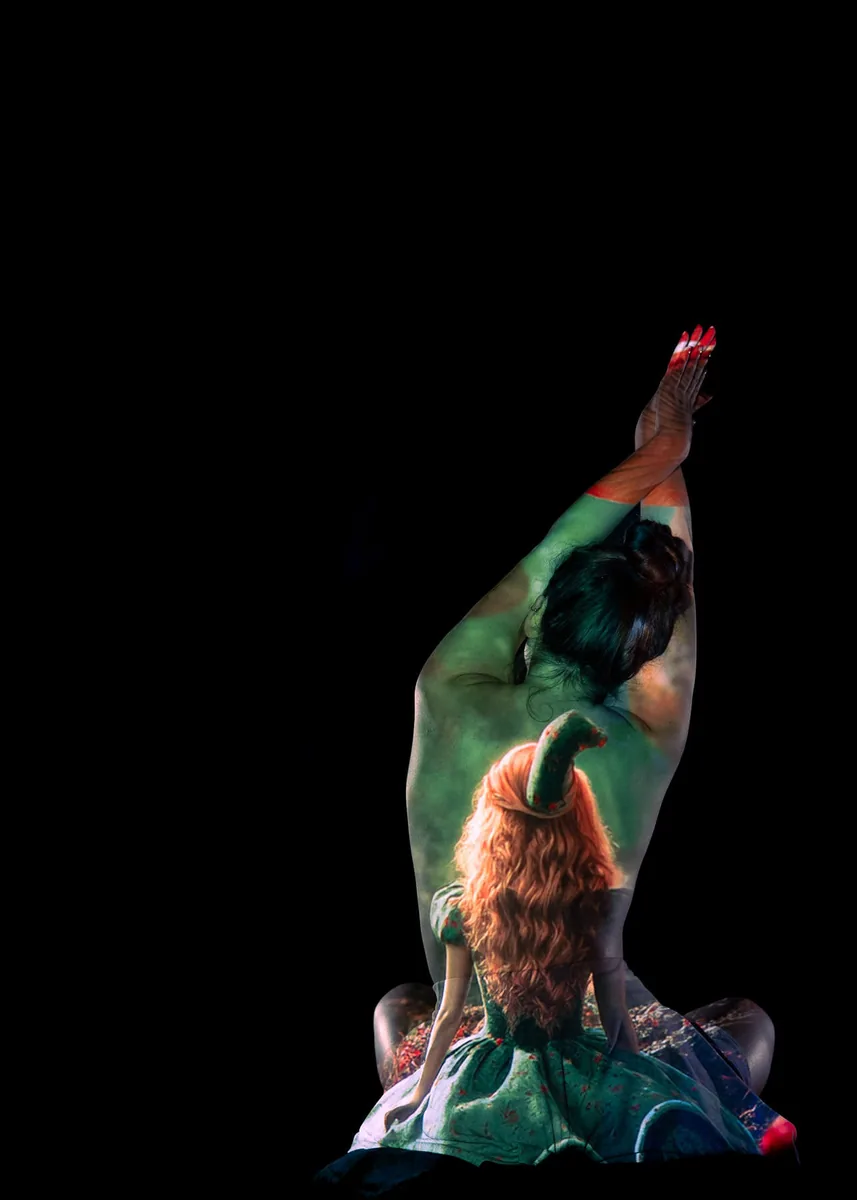 Person with back turned, arms raised, painted with detailed image of a doll in a green dress and hat on their back