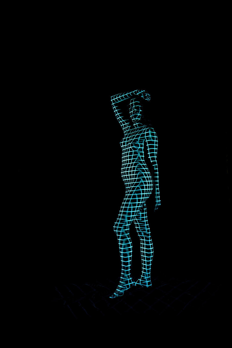 Nude figure standing with one arm raised, body covered in glowing blue grid lines against a dark background