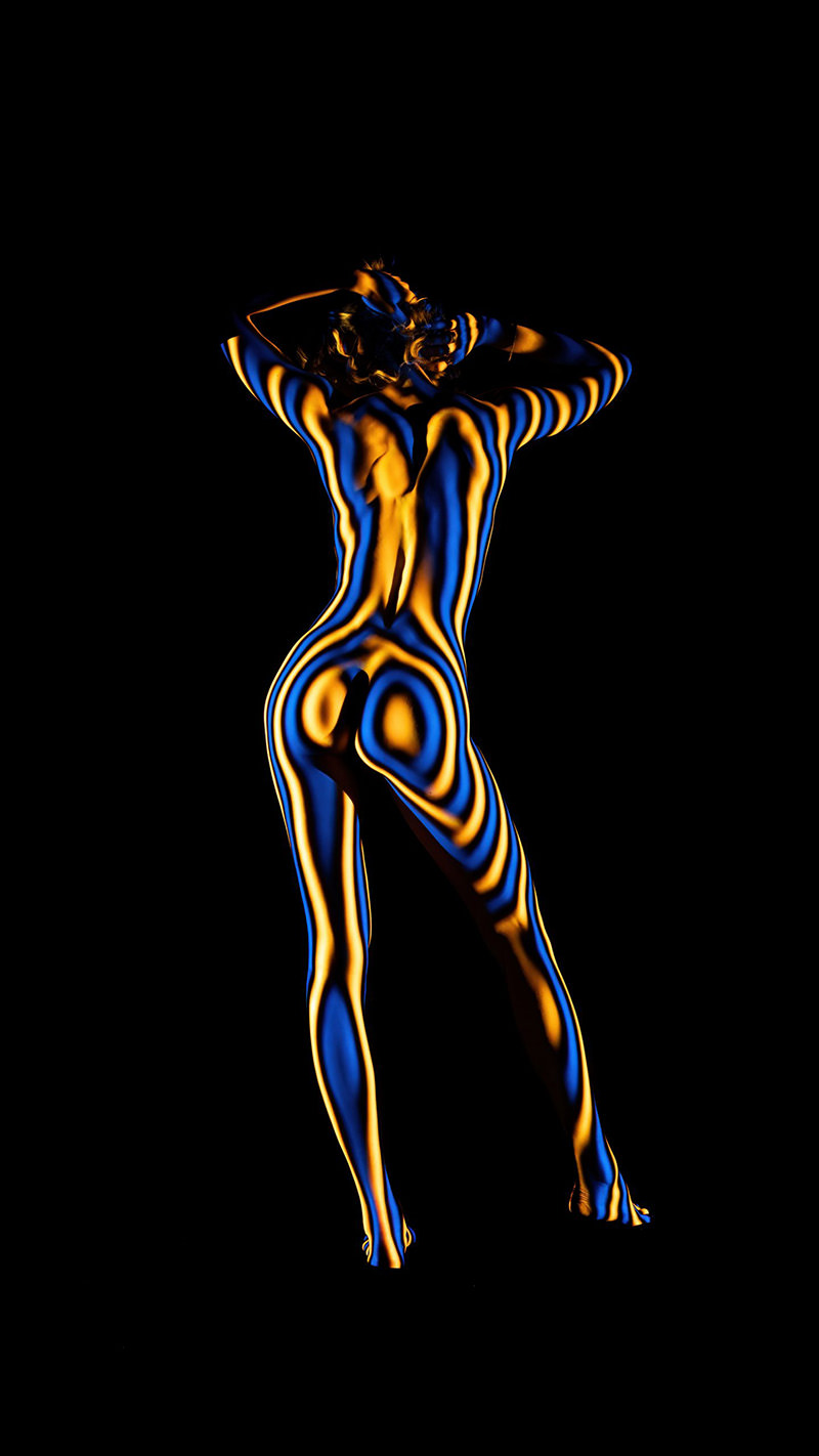 Back view of a nude person with blue and orange light stripes projected onto their body, standing against a black background with arms raised and hands near the head