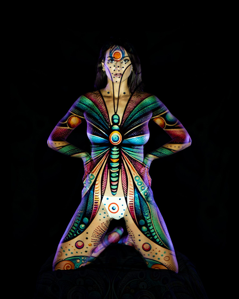 Woman with vibrant butterfly body paint standing with hands on hips against a black background