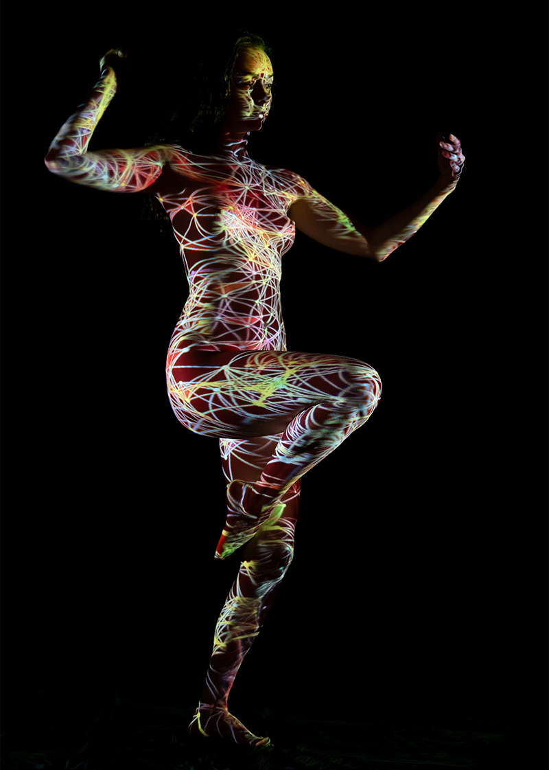 A person balancing on one leg, with intricate colorful light patterns projected across their body against a black background