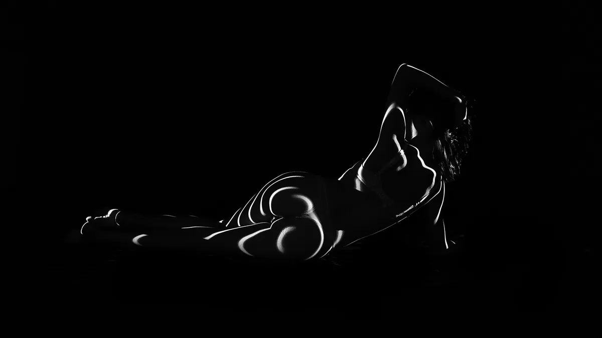 Person lying on their side with abstract curved white light patterns projected on their body against a black background