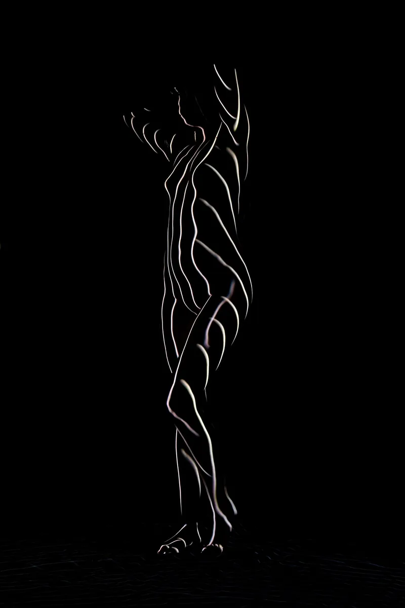Silhouette of a nude person outlined by glowing, curved light lines creating an abstract, artistic effect against a black background