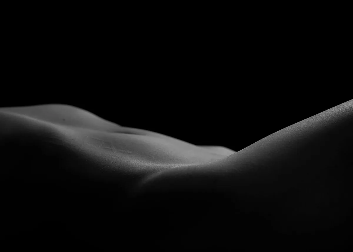 Close-up of a human torso with soft lighting emphasizing smooth curves and subtle shadows against a black background