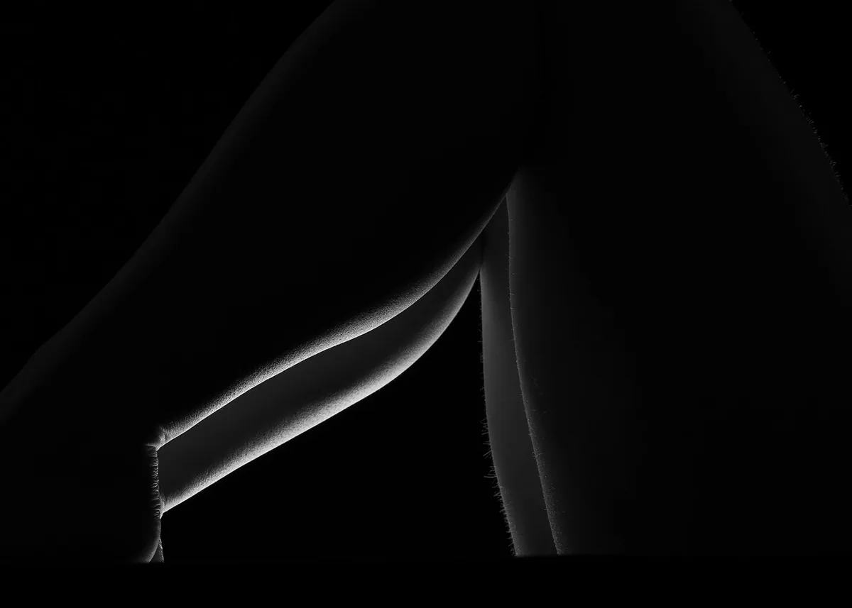 Close-up of bent legs with delicate backlighting emphasizing smooth skin texture and outlines against a black background