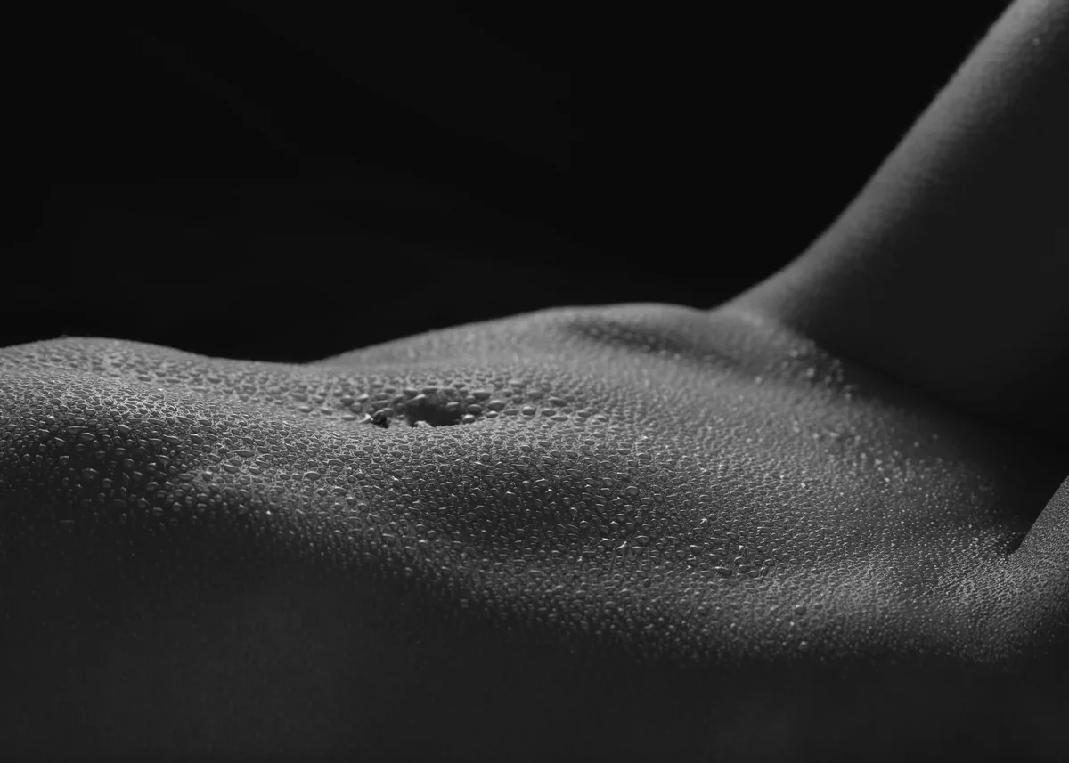 Black and white close-up of a torso with water droplets covering the skin, focusing on the belly button and subtle textures