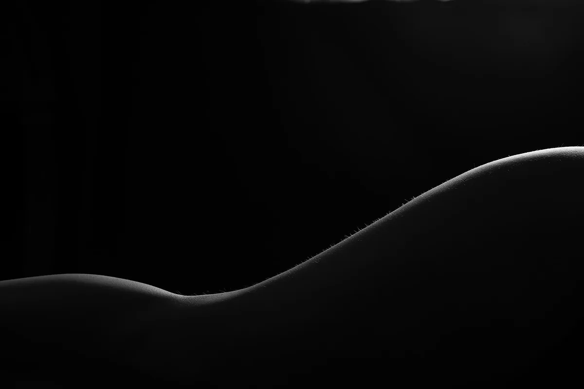 Curved human form highlighted by gentle light against a dark background