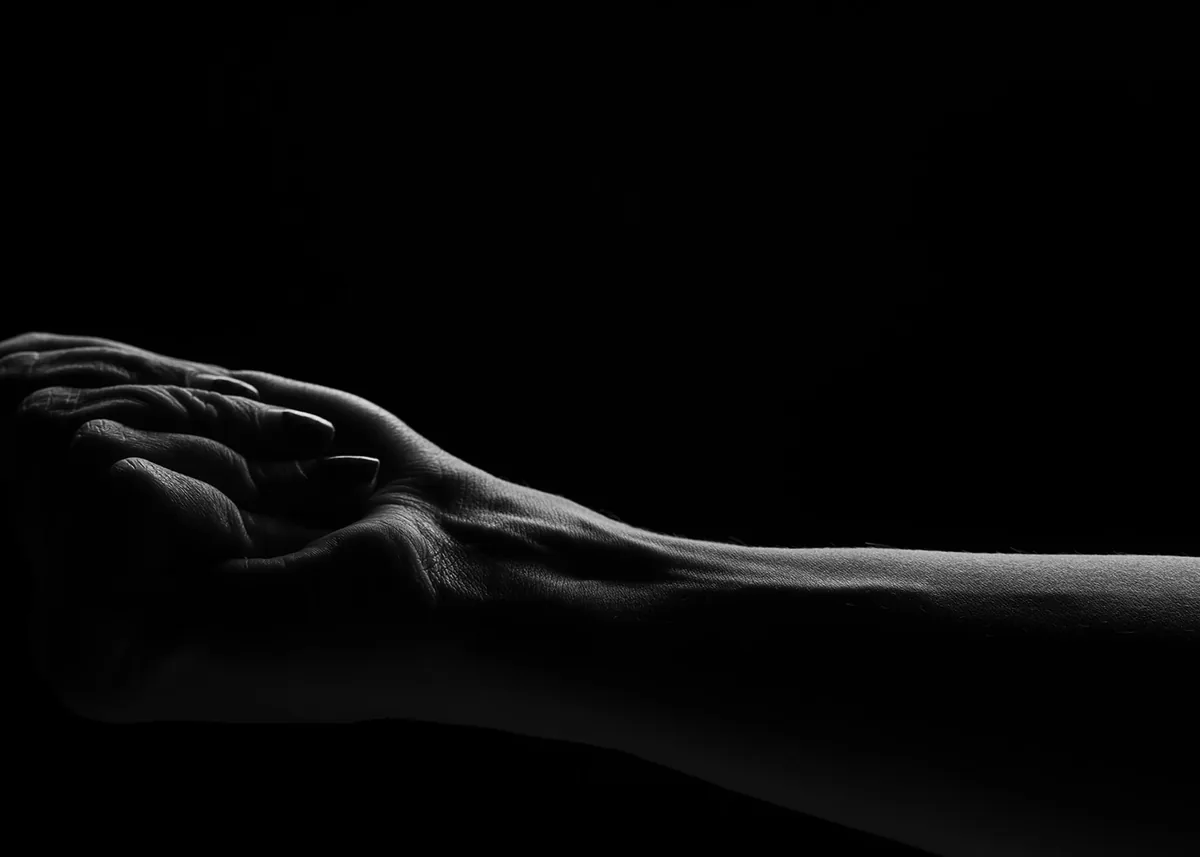 Close-up of two hands clasped together with visible veins and textures, lit dramatically against a black background