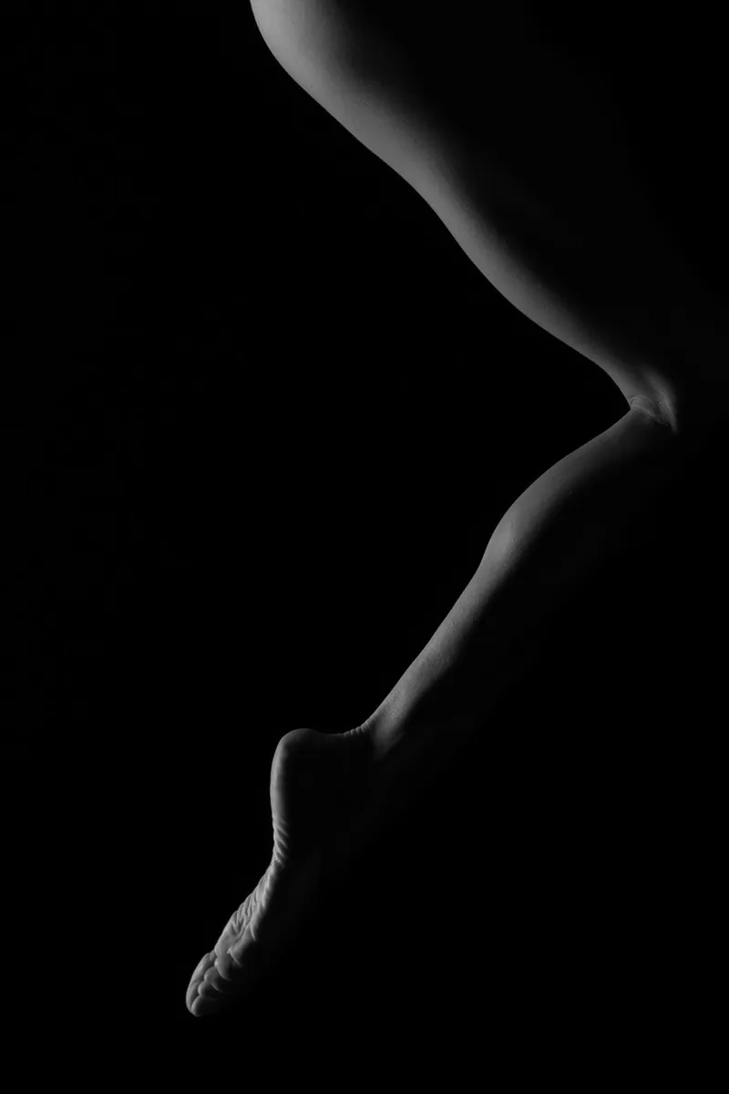 Close-up of a bent human leg and foot illuminated gently against a black background