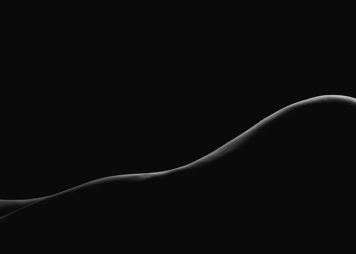 Curved silhouette of a reclining human body against a black background, highlighted by soft edge lighting