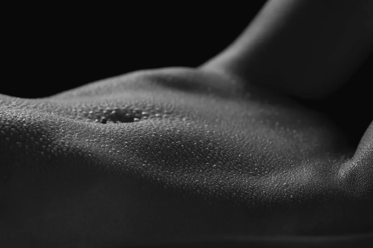 Close-up of a muscular abdomen covered in water droplets against a dark background