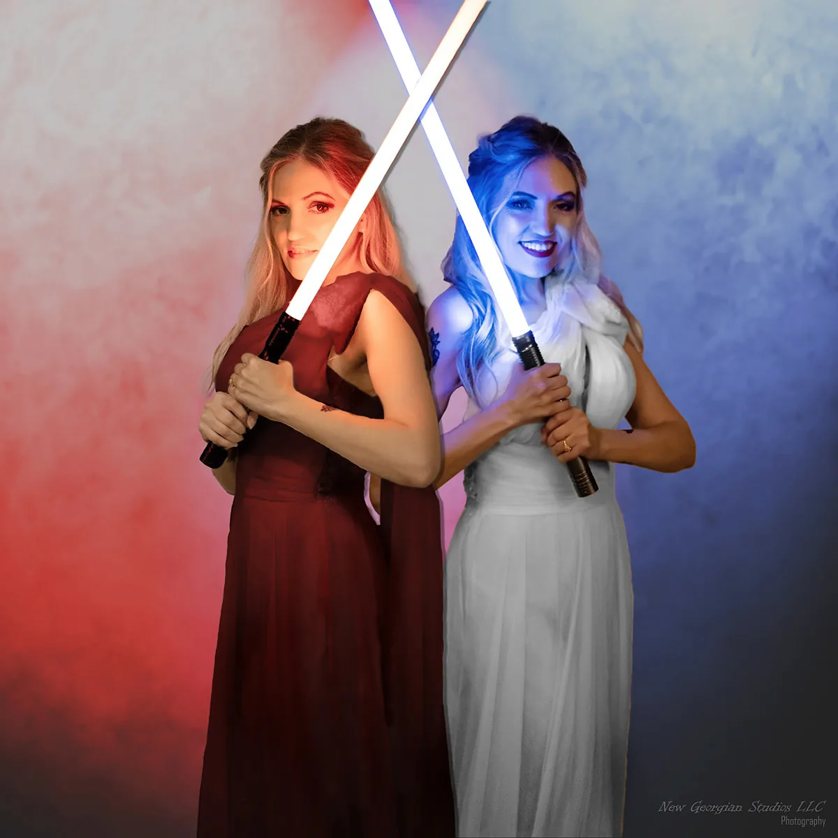 Two women back-to-back holding crossed lightsabers, one in a red dress with red lighting, the other in a white dress with blue lighting, both smiling.