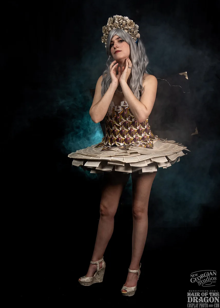 Woman wearing a unique dress made of printed paper pages and cards, paired with a crown of beige roses and wavy silver hair, standing against a dark smoky background